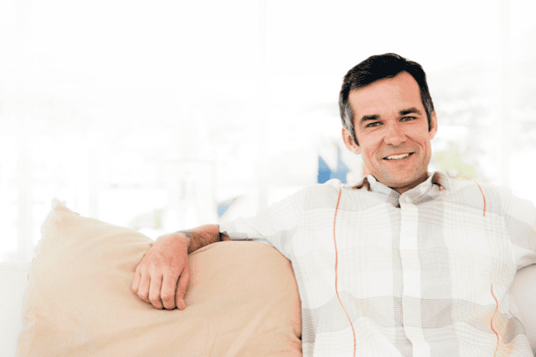 A confident man relaxing on a beige sofa in a bright, modern living room, showcasing comfort and style with natural light.