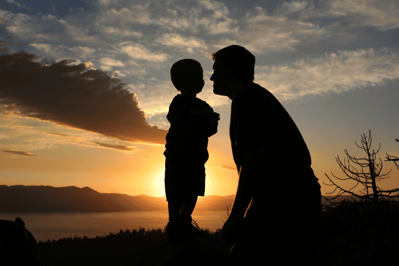 Silhouette of father and child sharing a tender moment at sunset, mountain landscape in background, emotional father and son bond, outdoor family photography, peaceful evening scene.