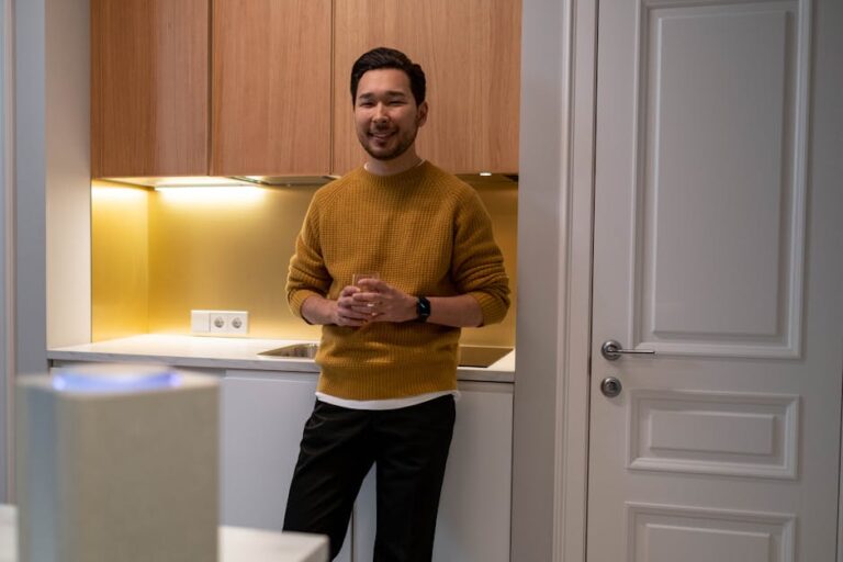 A man smiles in a modern kitchen, featuring a smart speaker on the counter.