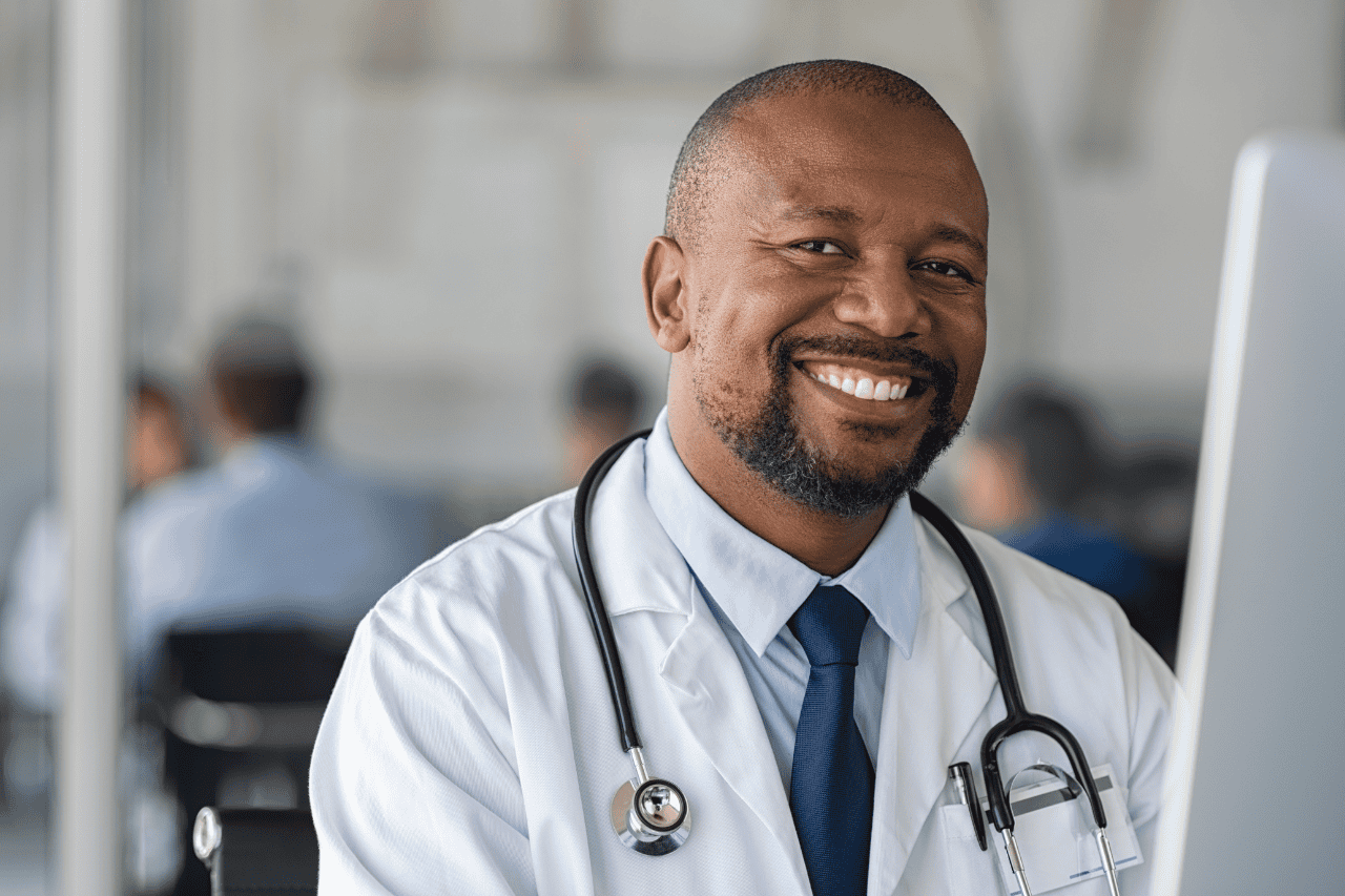 Compassionate male doctor smiling in hospital setting, wearing white coat and stethoscope, showcasing professionalism and care in healthcare.