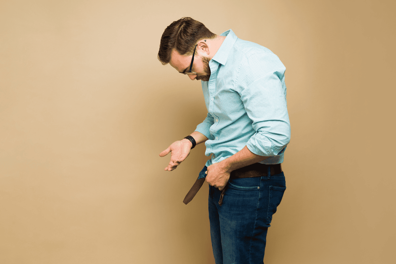 Frustrated man looking at empty pockets, financial stress, money problems, economic difficulties, personal finance issues.