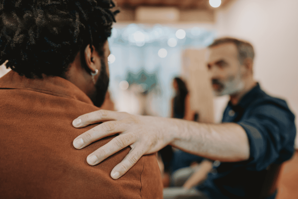 Supportive man comforting a troubled friend, emphasizing empathy and friendship, informal indoor setting, warm lighting, candid moment, focus on human connection, The Solemn Sir key theme.