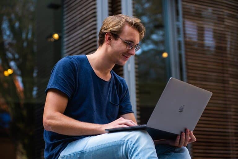Laptop user working outdoors, casual young man using a computer for remote work or leisure, modern environment, focused on technology and lifestyle.