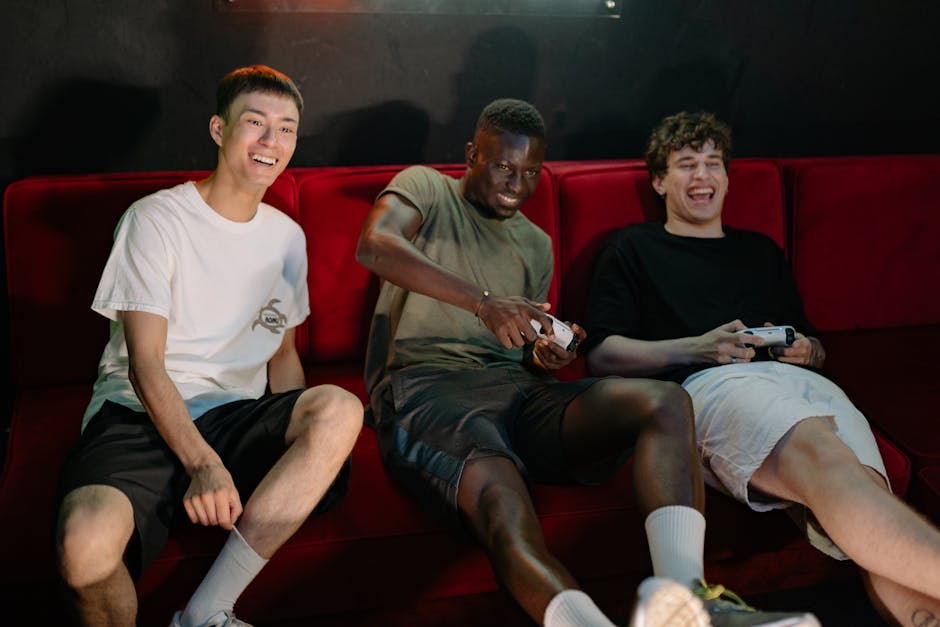 Happy young men playing video games together on a red sofa, casual gaming, fun social activity, The Solemn Sir gaming lounge, diverse group, entertainment and leisure, modern gaming setup, friendship, youth culture.