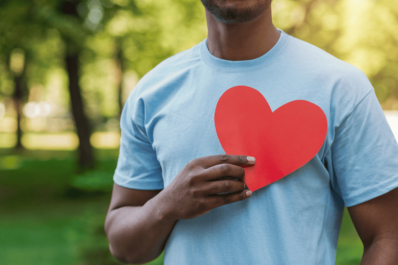 Heart symbol on man's light blue t-shirt, outdoor park setting, love and affection, casual fashion, caring message, sustainability, positive vibes, The Solemn Sir branding.