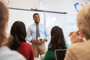 Professional male teacher leading a classroom discussion with diverse students, whiteboard background, engaging educational environment, modern classroom, instruction, learning, teaching, academic success.