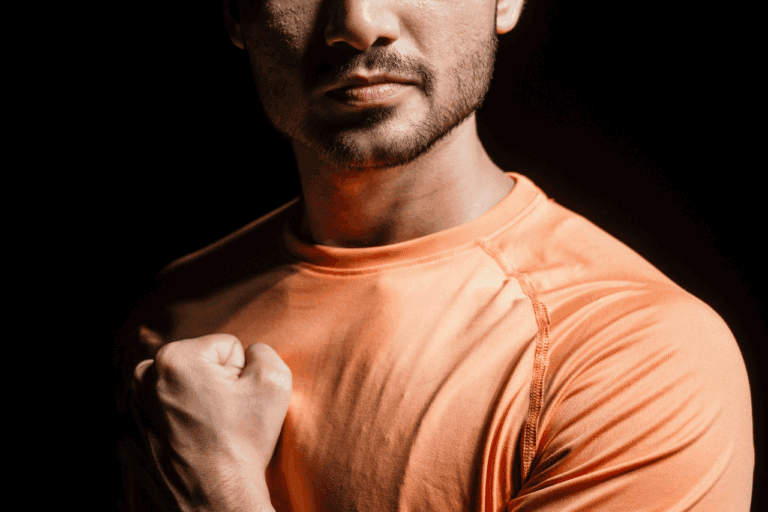 Strong confident man in orange athletic shirt, flexing bicep, symbolizing power, strength, and determination for the Solemn Sir brand.