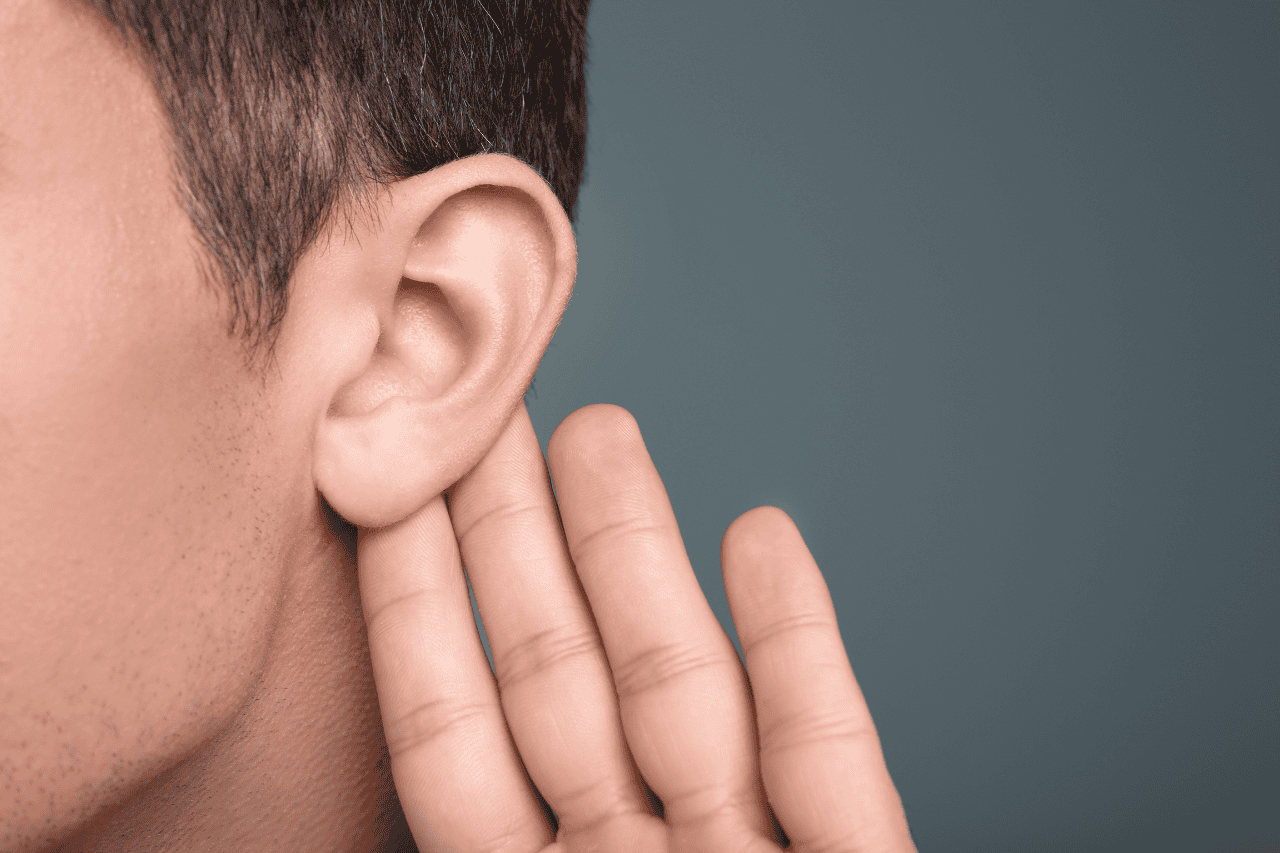 Hearing aid or ear health concept, close-up of a person placing their hand behind the ear, emphasizing auditory care and wellness.