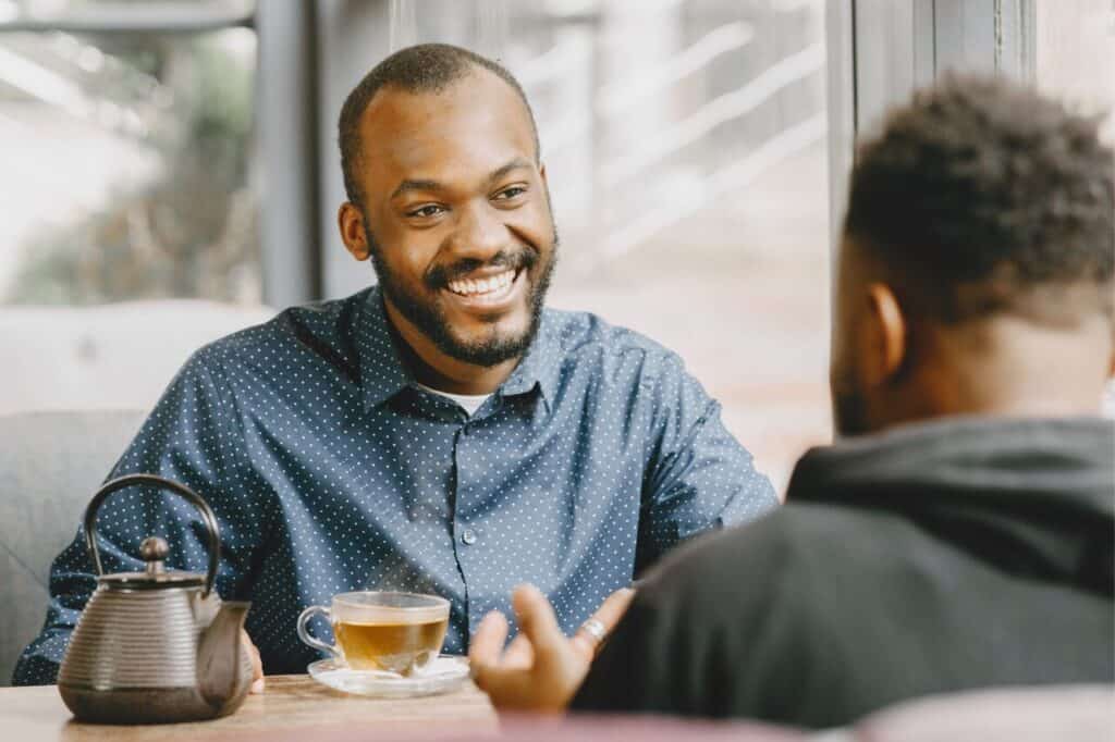 Friendly man smiling during a conversation in a cozy cafe with tea on the table, emphasizing relaxed social interaction and warm atmosphere for lifestyle and coffee shop SEO.