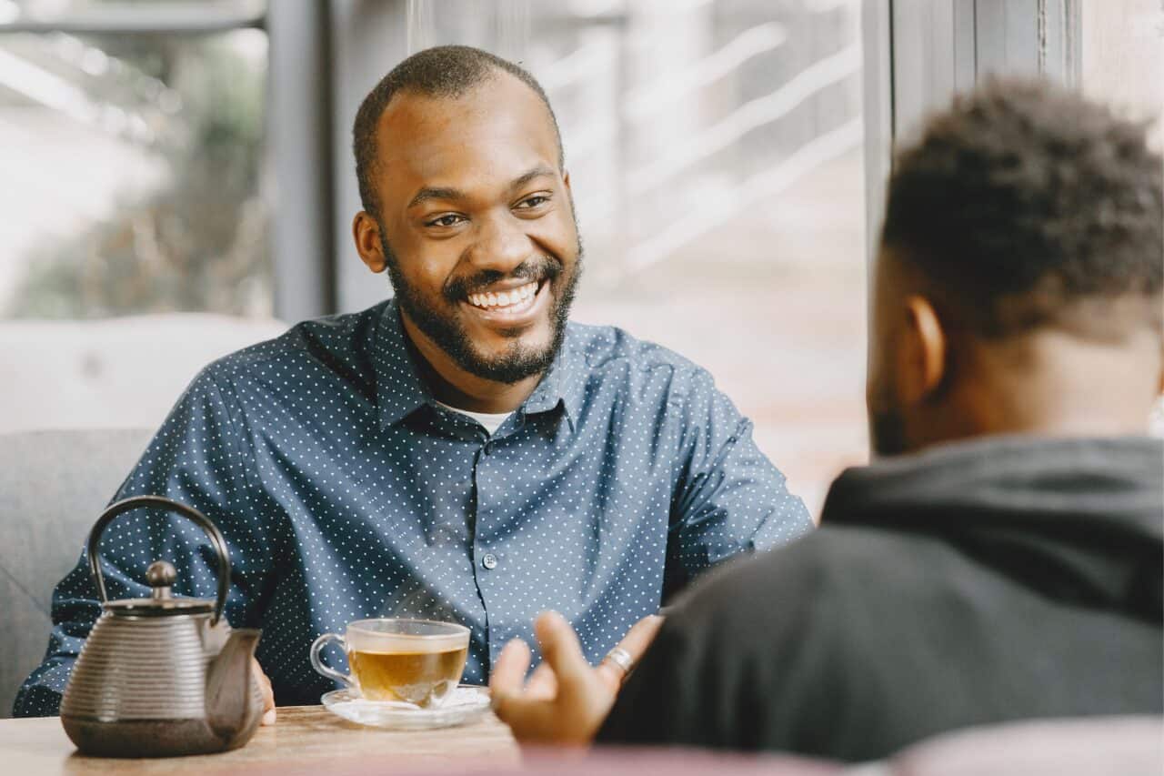 Friendly man smiling during a conversation in a cozy cafe with tea on the table, emphasizing relaxed social interaction and warm atmosphere for lifestyle and coffee shop SEO.