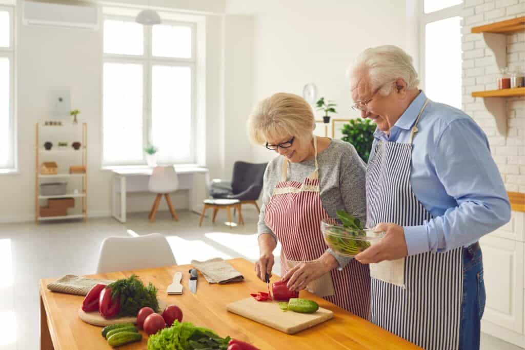 Fresh elderly couple preparing vegetables in bright modern kitchen for healthy cooking.