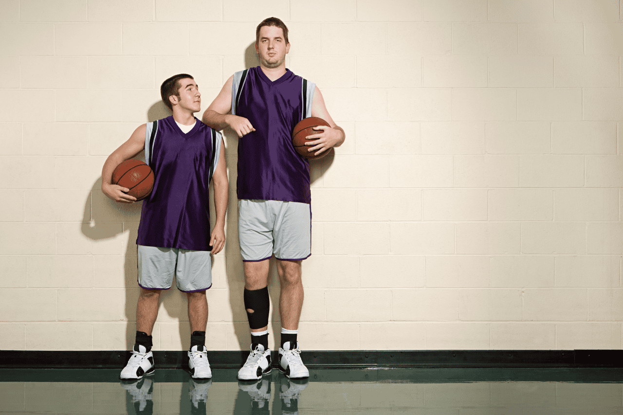 Teenage boys basketball players in purple jerseys standing against a gym wall with basketballs in hand.