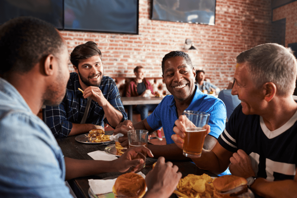 A group of diverse friends enjoying beers and burgers at a rustic restaurant, sharing laughs and good times, showcasing camaraderie, casual dining, and vibrant social atmosphere.