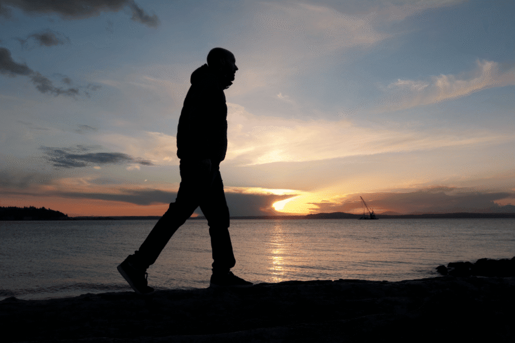 Silhouette of a man walking along the beach at sunset, reflecting calm and solitude, perfect for introspective or relaxation-themed content.