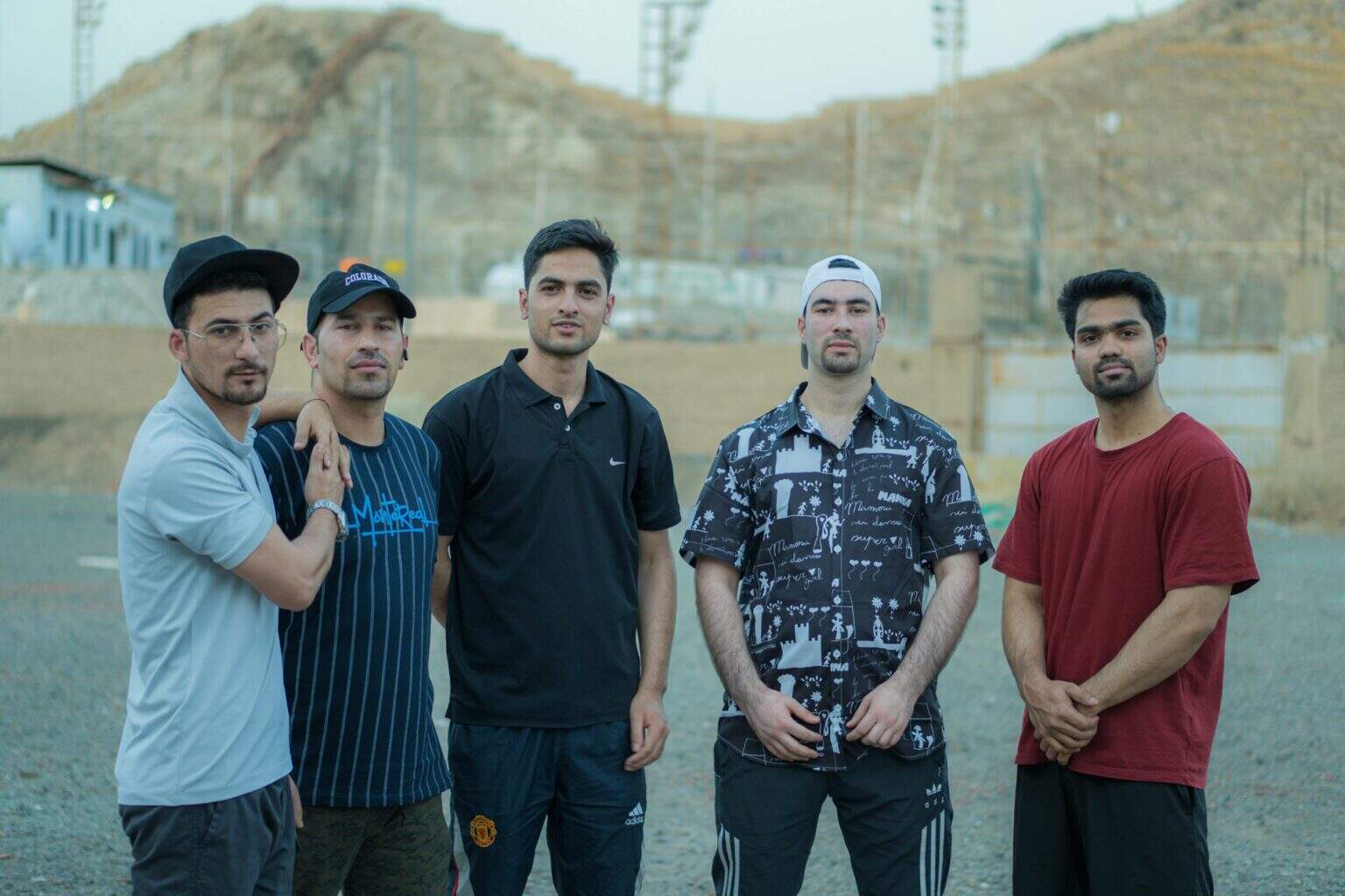 Five young men posing together outdoors, showcasing casual fashion and friendship.