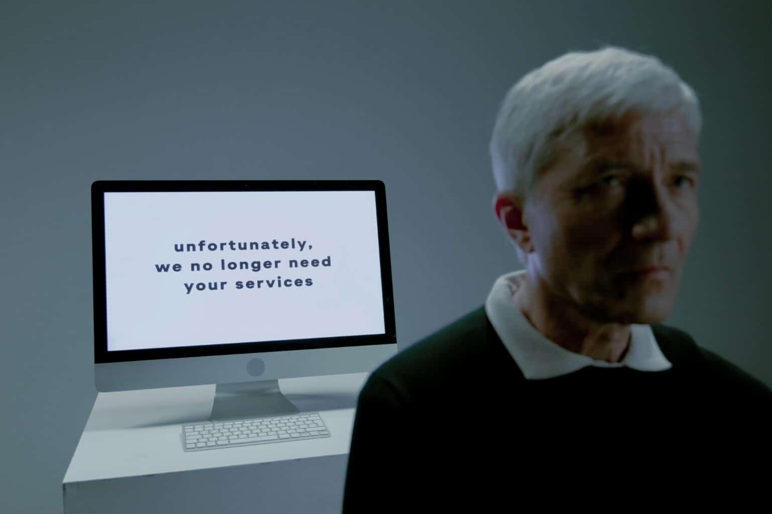 Senior man looks away from an unemployment notice on a computer screen indoors.