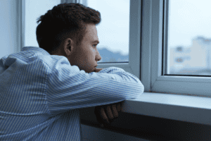 A man looking out the window with a contemplative expression, symbolizing loneliness and the challenge of building genuine friendships as a man.