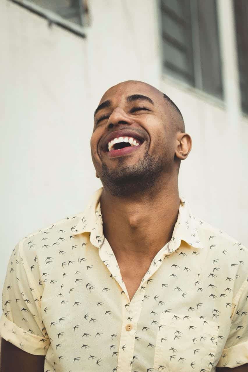 A cheerful man in a patterned shirt smiling joyfully outdoors.